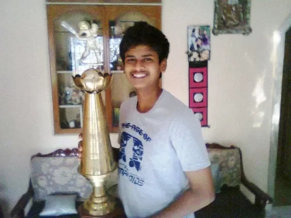 Young Shreyas Iyer smiling beside a large cricket trophy at home