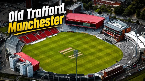 Aerial view of Old Trafford cricket ground in Manchester, showing the green pitch, stands, pavilion buildings, floodlights, and surrounding city area.