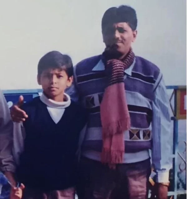 Childhood photo of Suryakumar Yadav standing beside an elder family member during his early years.