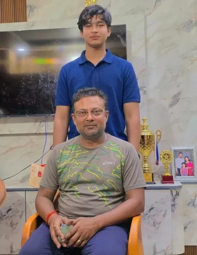 Vaibhav Sooryavanshi stands with his cricket coach Manish Ojha beside trophies and awards.